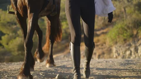 Front view legs of unrecognizable horse and woman strolling in slow motion on dusty mountain road