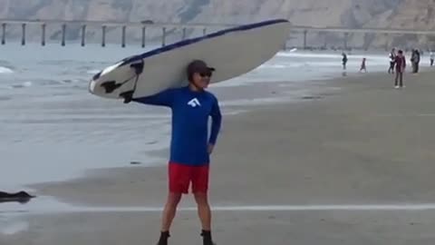 Man in blue carrying white surfboard for picture