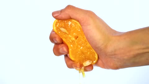 Hand of a person squeezing an orange on a light background