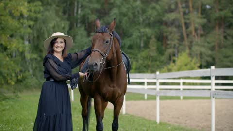 Beautiful woman in hat with brown horse on farm ranch