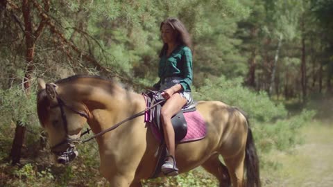 Positive beautiful black female rider riding on horseback on rural dusty road through forest