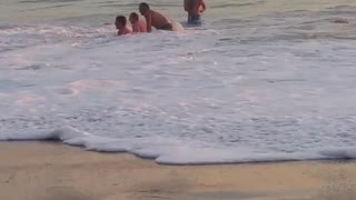 Several guys in the water keep getting knocked down by the waves