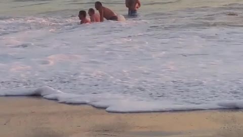 Several guys in the water keep getting knocked down by the waves