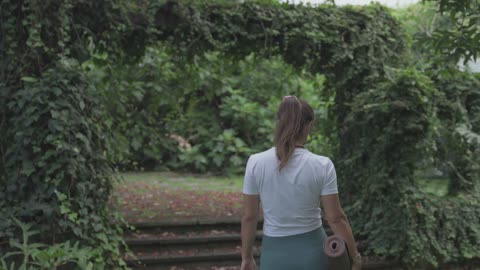 Woman walking in a park while holding a yoga mat