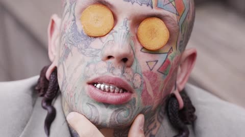 Tattooed Man Posing with Carrot Slices on Eyes