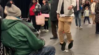 Guy dances to man playing harmonica in subway station