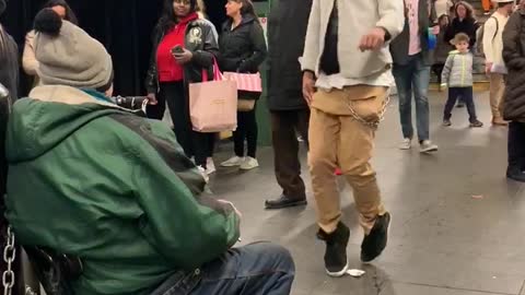 Guy dances to man playing harmonica in subway station