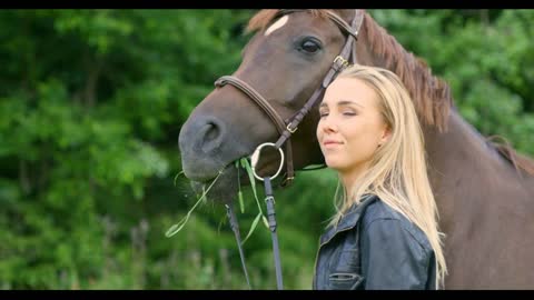 Smiling woman caressing and feeding her arabian horse in the field