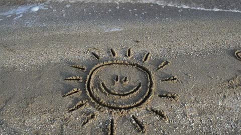 Smiling sun drawn in the sand on a beach