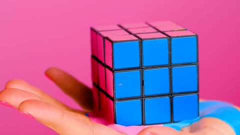 Hand holding a rubik cube that seems to melt on a pink background