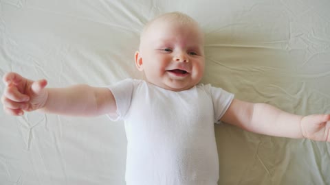 Happy baby lying on white bed in white shirt