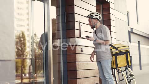 Food Delivery Man Wearing Thermal Backpack Calls The Entry Phone Of A Building To Make A Delivery