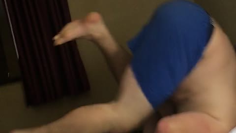 Shirtless guy in blue shorts does a flip in bed and farts