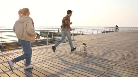 Cheerful young couple runnung and playing with cute Jack Russel terrier dog outdoors near the sea