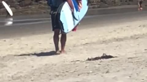 Guy with backpack puts towel on surfboard