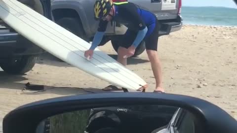 Yellow helmet guy waxes white surfboard out of back car