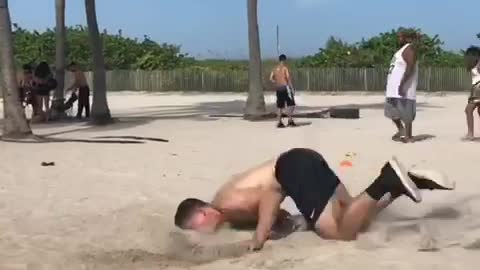 Shirtless man black shorts back flip fail in beach sand