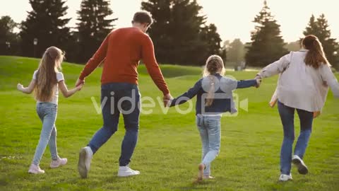 Back View Of Happy Family Holding Hands And Running Together In The Park