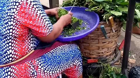 African Woman Cutting Fresh Pumpkin Leaves In The Market