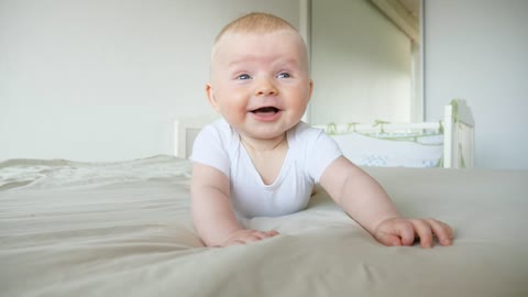 Cute laughing baby rolls over on bed