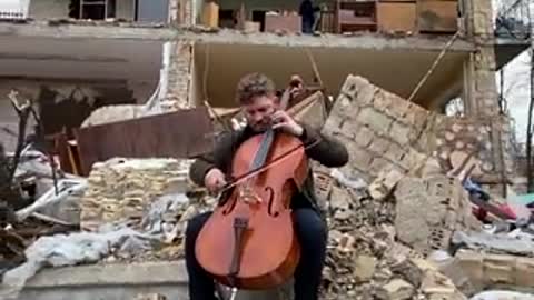 A young cellist playing on the ruins of his house