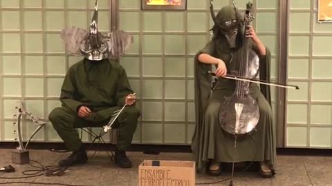 Two people in silver animal masks play instruments