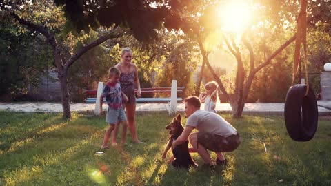 young parents playing with puppy dog and children at park with sunlight shining over small trees