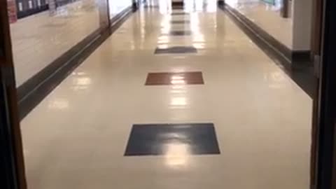 Guy in blue shirt running down hallway trips on trash can