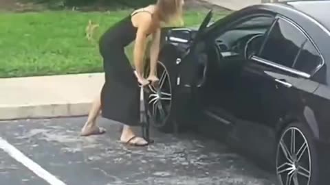 chick tries to get her car started by pumping the tyre up.