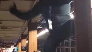 Man climbs and hangs on the side of pillar in subway train