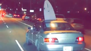 Brown car drives on road with surfboard sticking out of sunroof