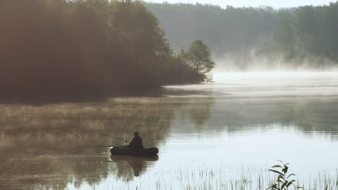 A person fishing on a boat on a misty early morning