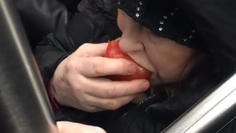 Woman eats a whole tomato on subway train