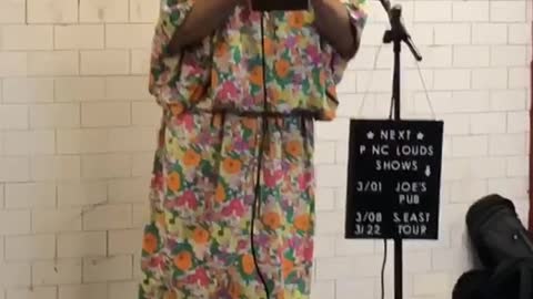 Man dressed up in makeup, wig, and large floral dress performs and sings in a subway station