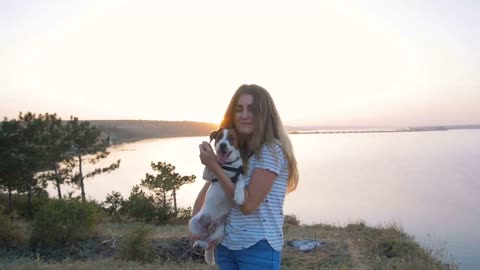 Young attractive woman playing with a dog Jack Russell in the meadow at sunset with sea background