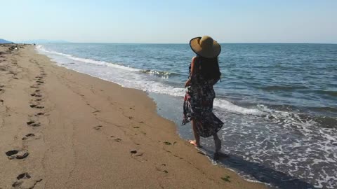 Woman with a hat walking on an empty beach