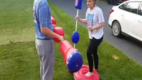 Girl and guy fighting on red and blue inflatable platforms fighting with blow up baton sticks