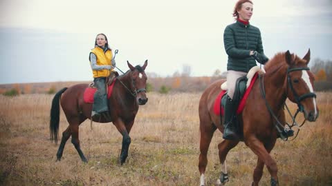 Two women are riding horses which are grazing on the field