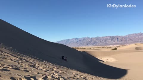 Two people slide down sand dune fall at bottom