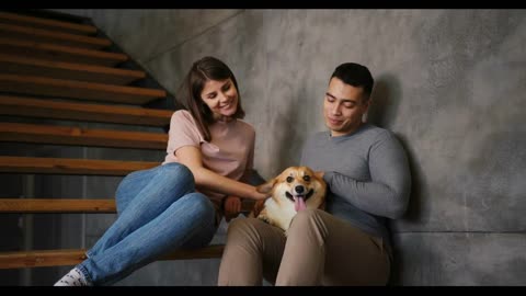 Positive young man and pretty woman pet fluffy corgi dog sitting on wooden