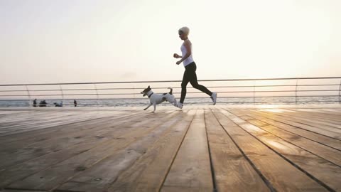 Young woman running with cute dog Jack Russel near the sea