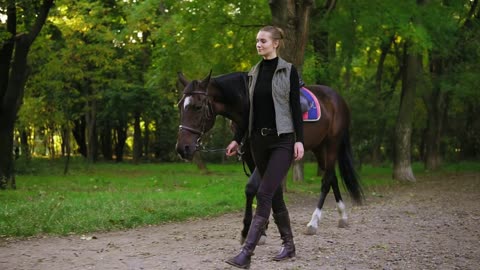 Young happy female horse rider is walking with brown horse with white