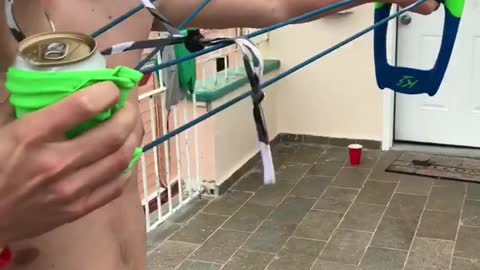 Guy shoots beer in green slingshot to friend