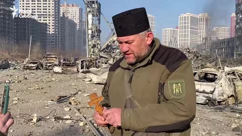 Chaplain Mykola Medynskiy reads a prayer next to the bombed-out shopping mall