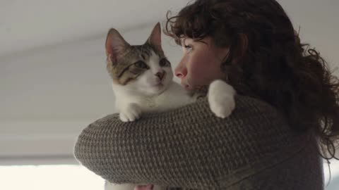 Beautiful young woman cradles cat in her arms while watching out her window
