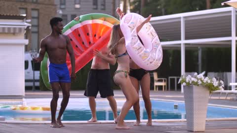 Friends dancing happily near a swimming pool