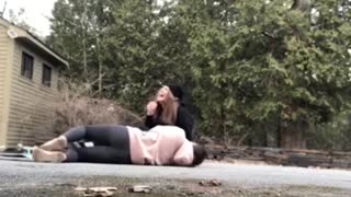 Two girls try to ride a skateboard together and fall off