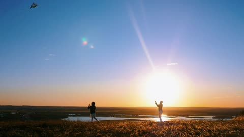 Man flying a kite and a girl running at sunset