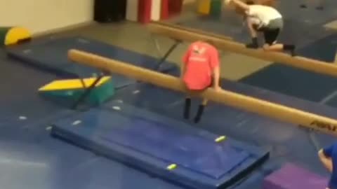 Red shirt kid hops on balance beam and falls backwards