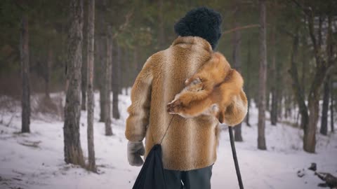 Live camera follows old Asian male hunter walking in woods in slow motion on winter day.